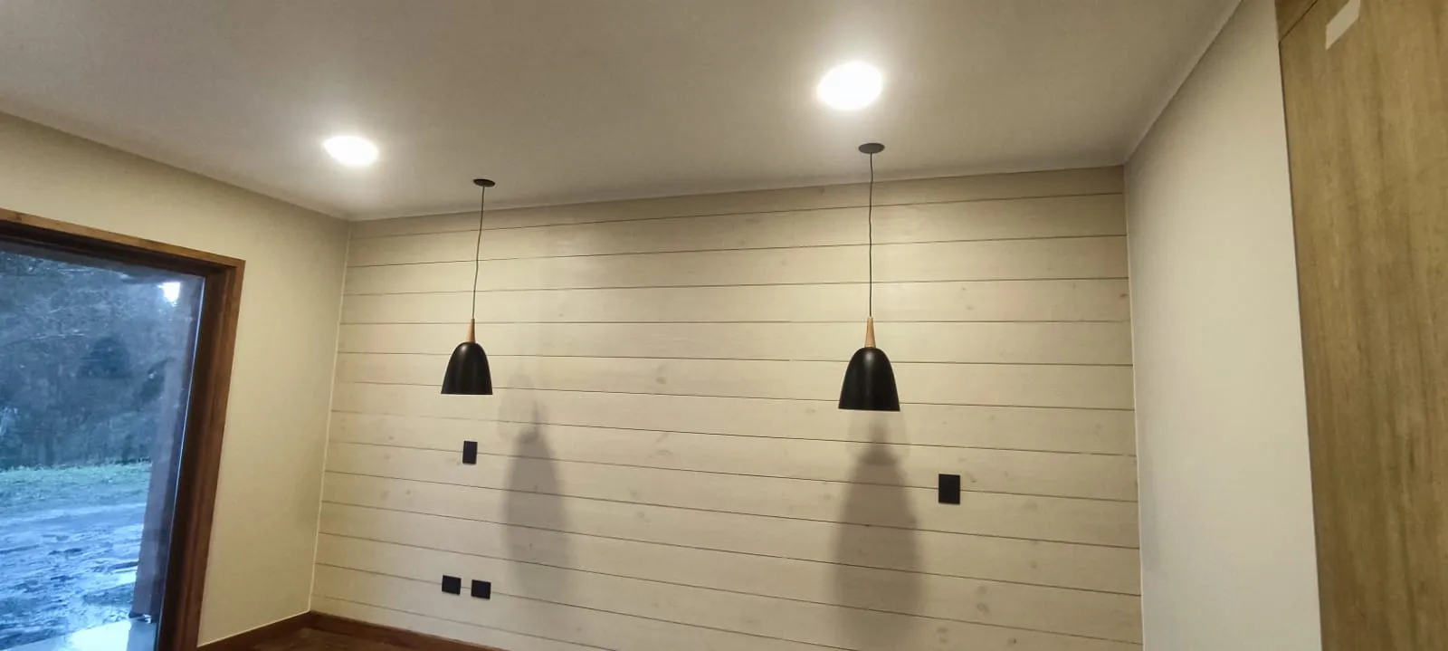 Lámparas colgantes negras sobre pared de madera en comedor de parcela